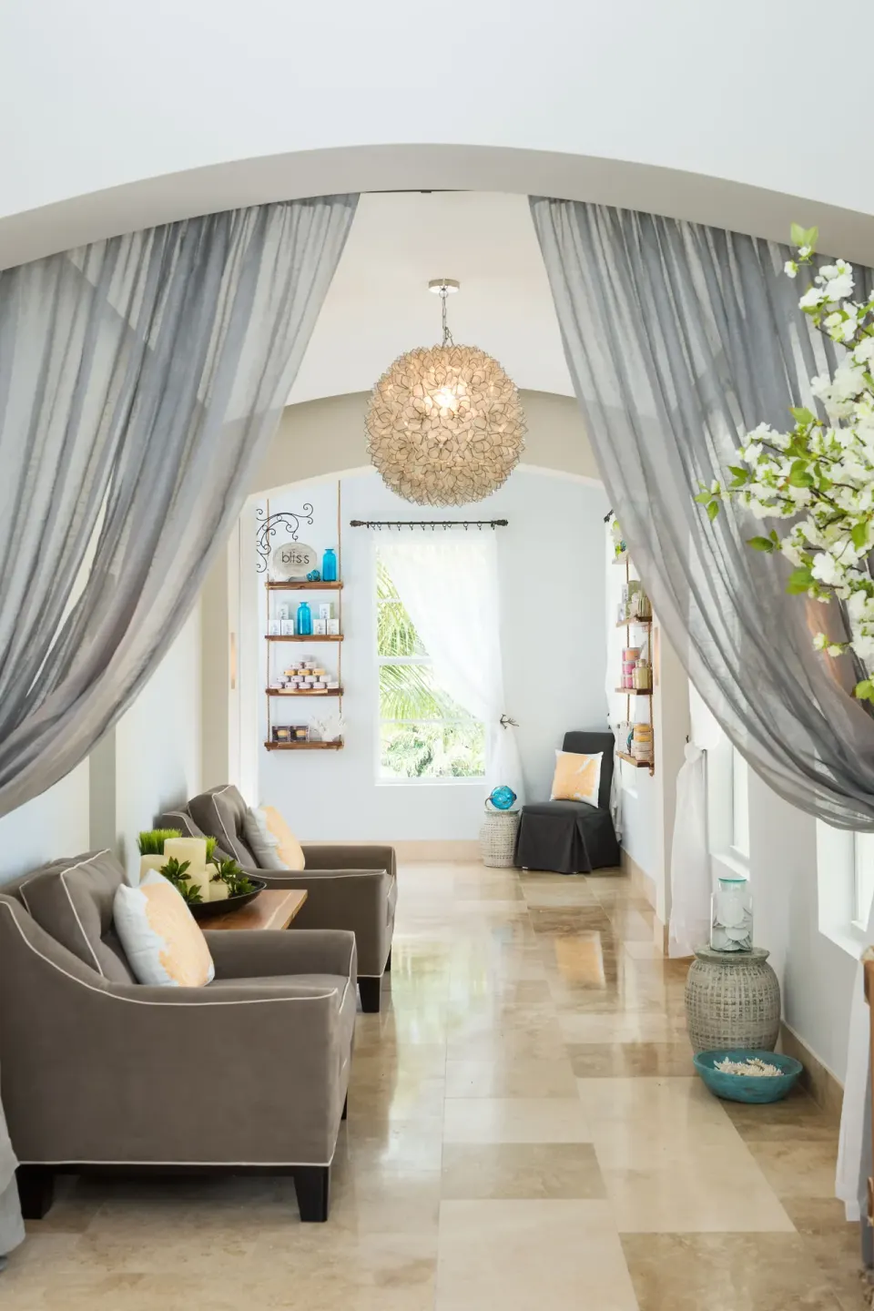 Spa lounge with gray drapes, armchairs, and a shell chandelier at Windsong on the Reef.