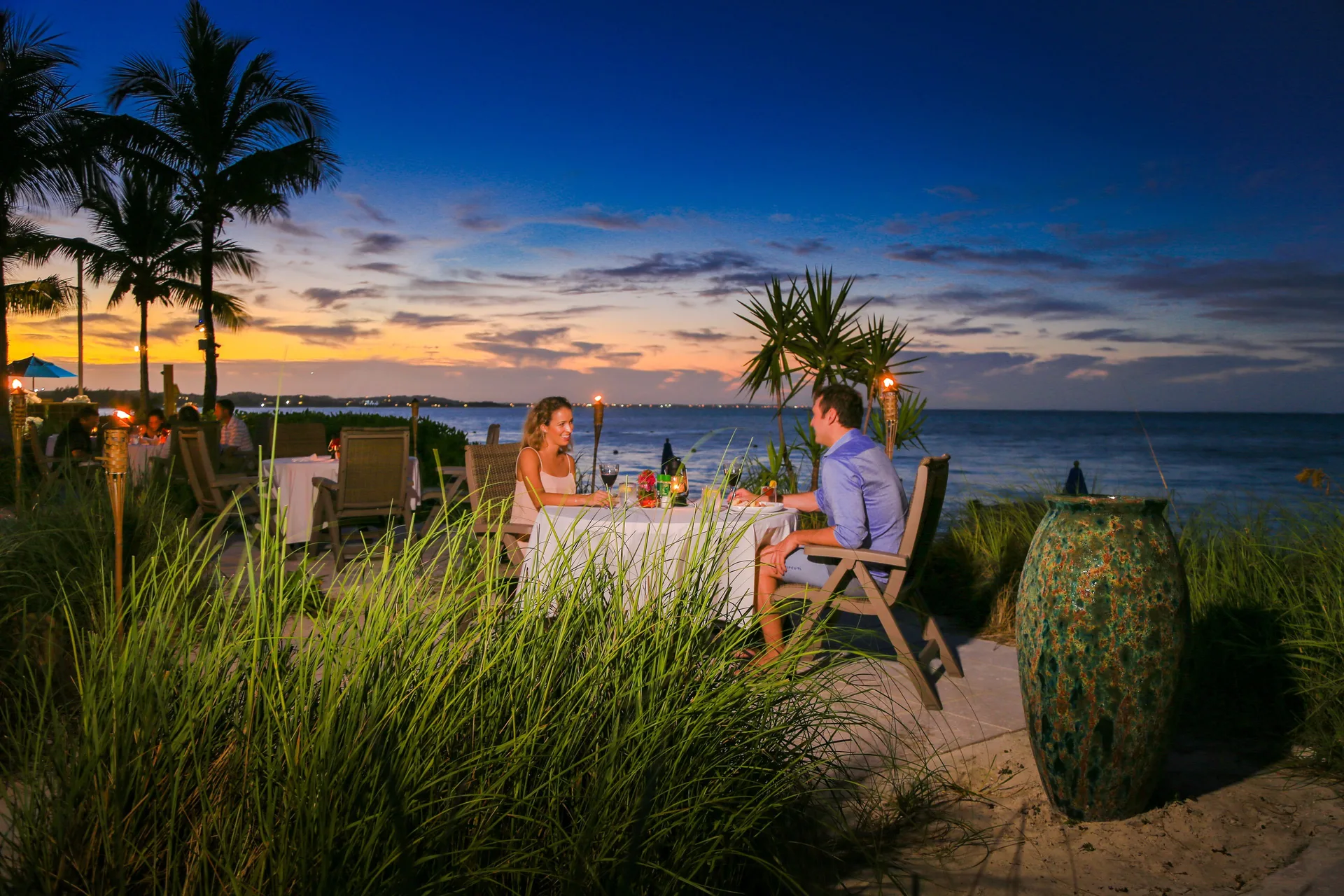Couple dining by the beach at sunset at Windsong on the Reef.