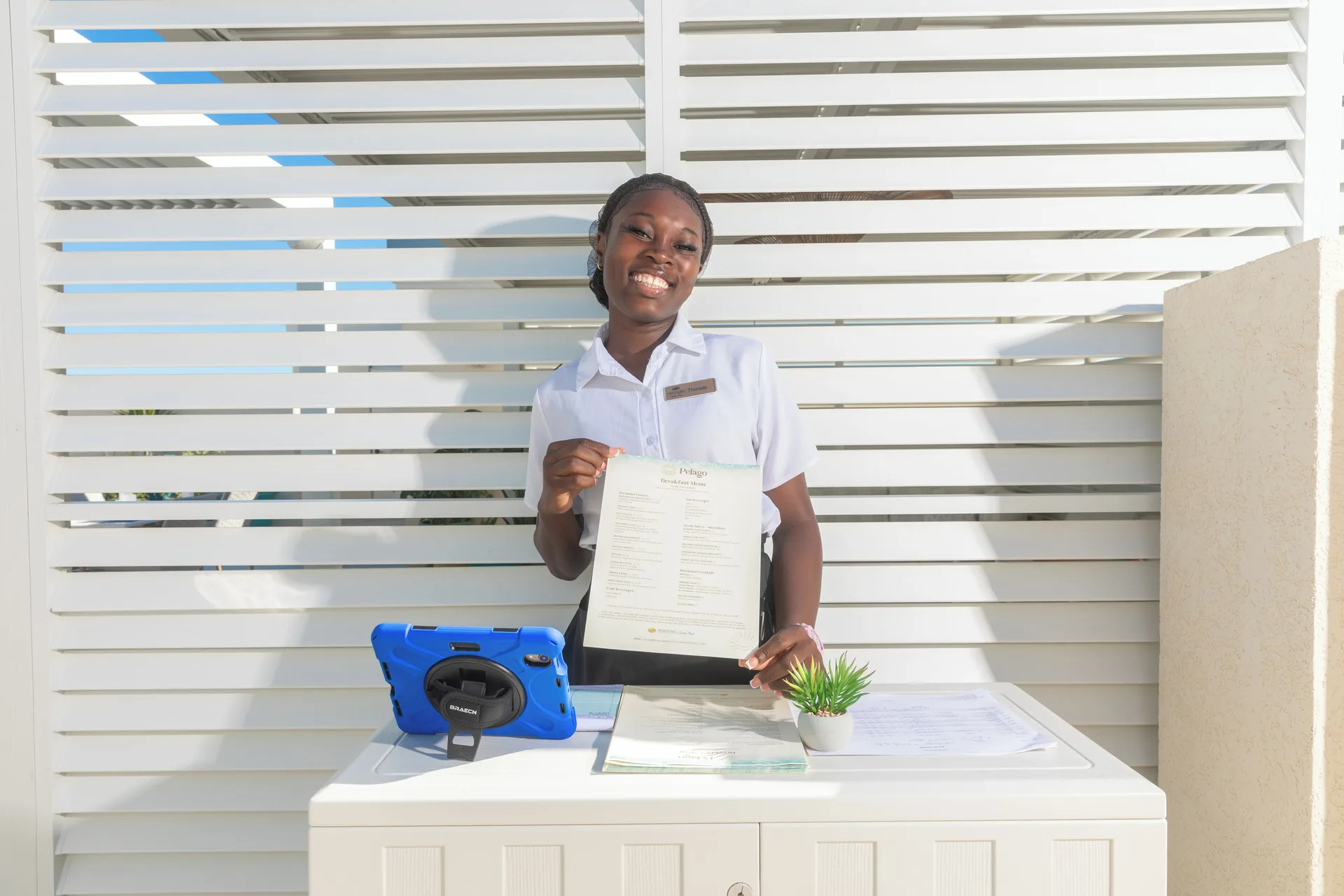 A smiling staff member holds a Pelago menu at Windsong on the Reef.
