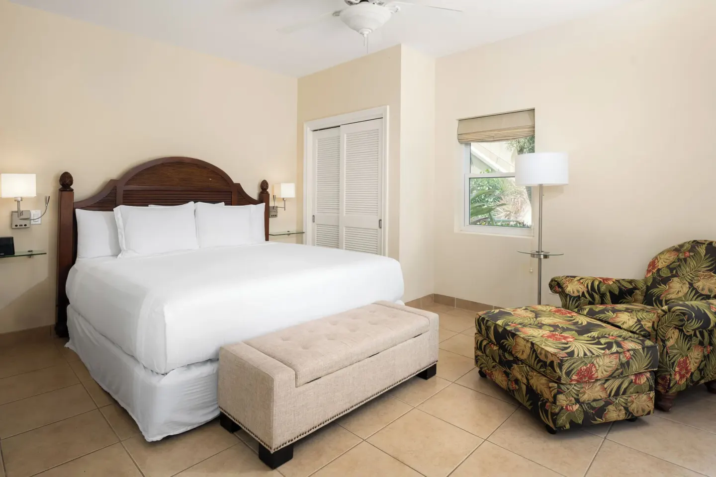 Bungalow bedroom with king bed, bench, and floral chair at Windsong on the Reef.