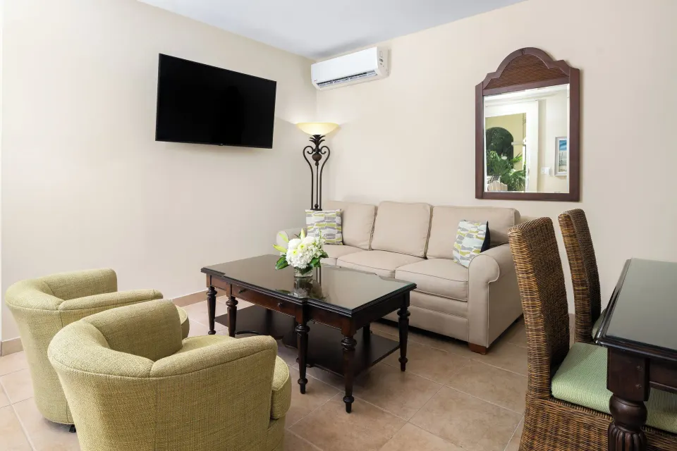 Bungalow living room with sofa, chairs, dining seats, and TV at Windsong on the Reef.
