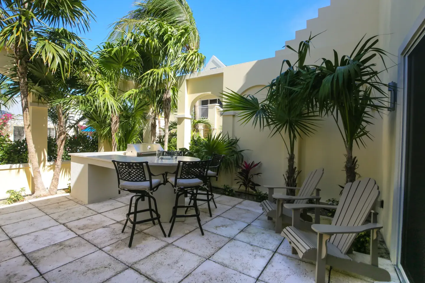 Two-bedroom bungalow lanai with grill, bar chairs, and palms at Windsong on the Reef.
