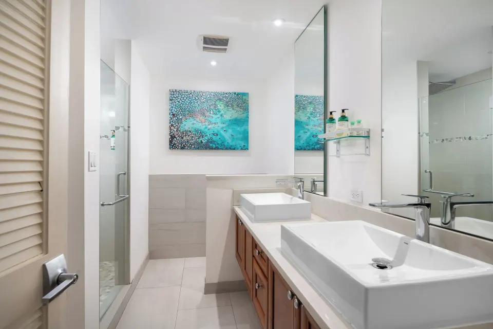 Bungalow bathroom with double vessel sinks and glass shower at Windsong on the Reef.