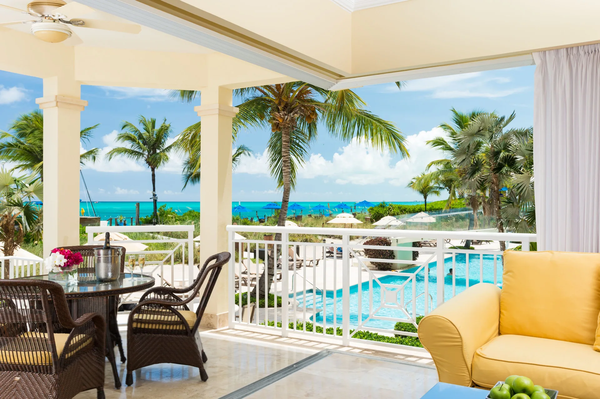 Oceanfront suite terrace with dining set, yellow sofa, pool, palms, and sea at Windsong on the Reef.