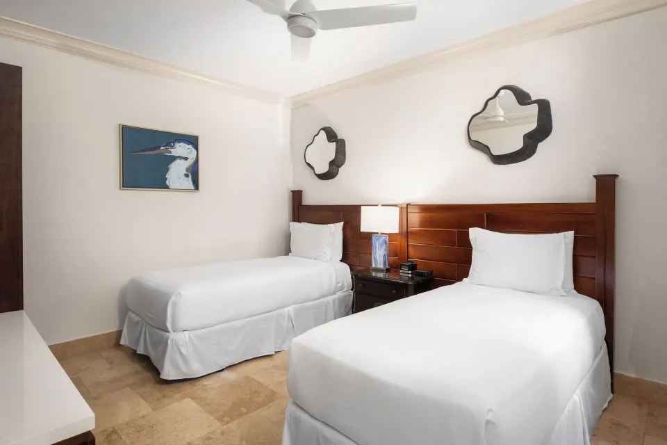 Twin bedroom with two white beds, mirrors, and bird artwork at Windsong on the Reef.
