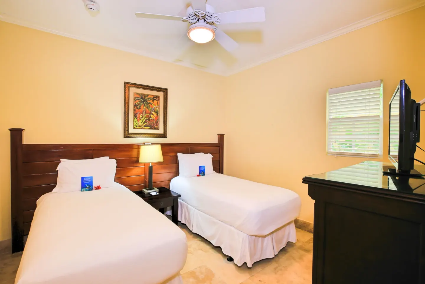 Twin bedroom with two white beds and TV in an oceanfront suite at Windsong on the Reef.