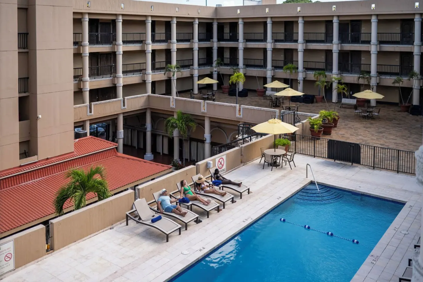 Courtyard pool with guests on loungers and umbrella seating at Windward Passage Hotel.