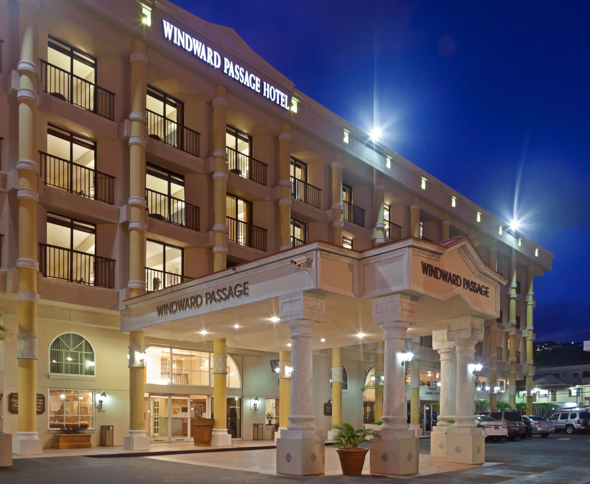 Illuminated hotel entrance and balconies at Windward Passage Hotel at night.