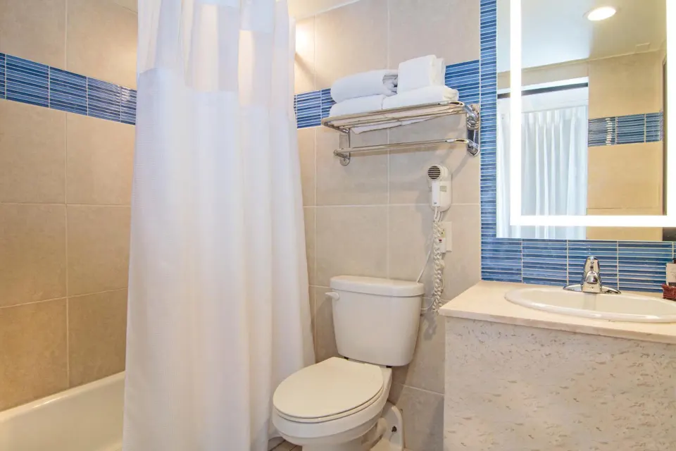 Standard Room bathroom with tub, toilet, sink, and lit mirror at Windward Passage Hotel.