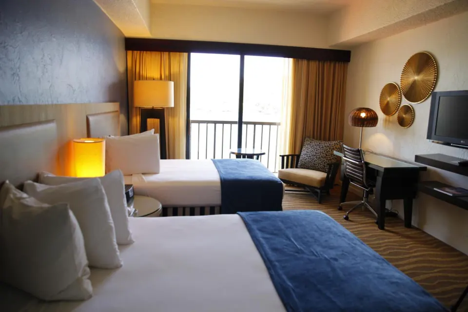 Standard Room with two beds, balcony doors, desk, and TV at Windward Passage Hotel.