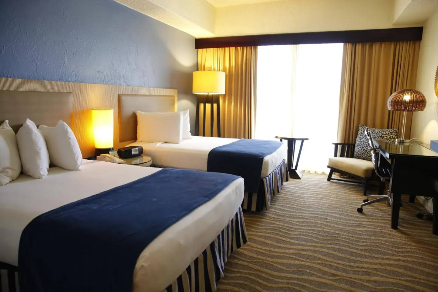 Standard Room with two beds, desk, chair, and curtains at Windward Passage Hotel.