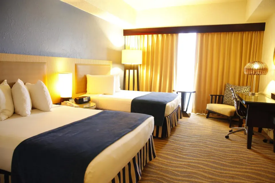 Standard Room with two beds and warm lighting by the window at Windward Passage Hotel.