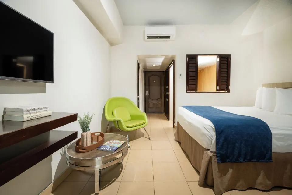 Standard Room with one bed in view, green chair, TV shelf, and entry hall at Windward Passage Hotel.