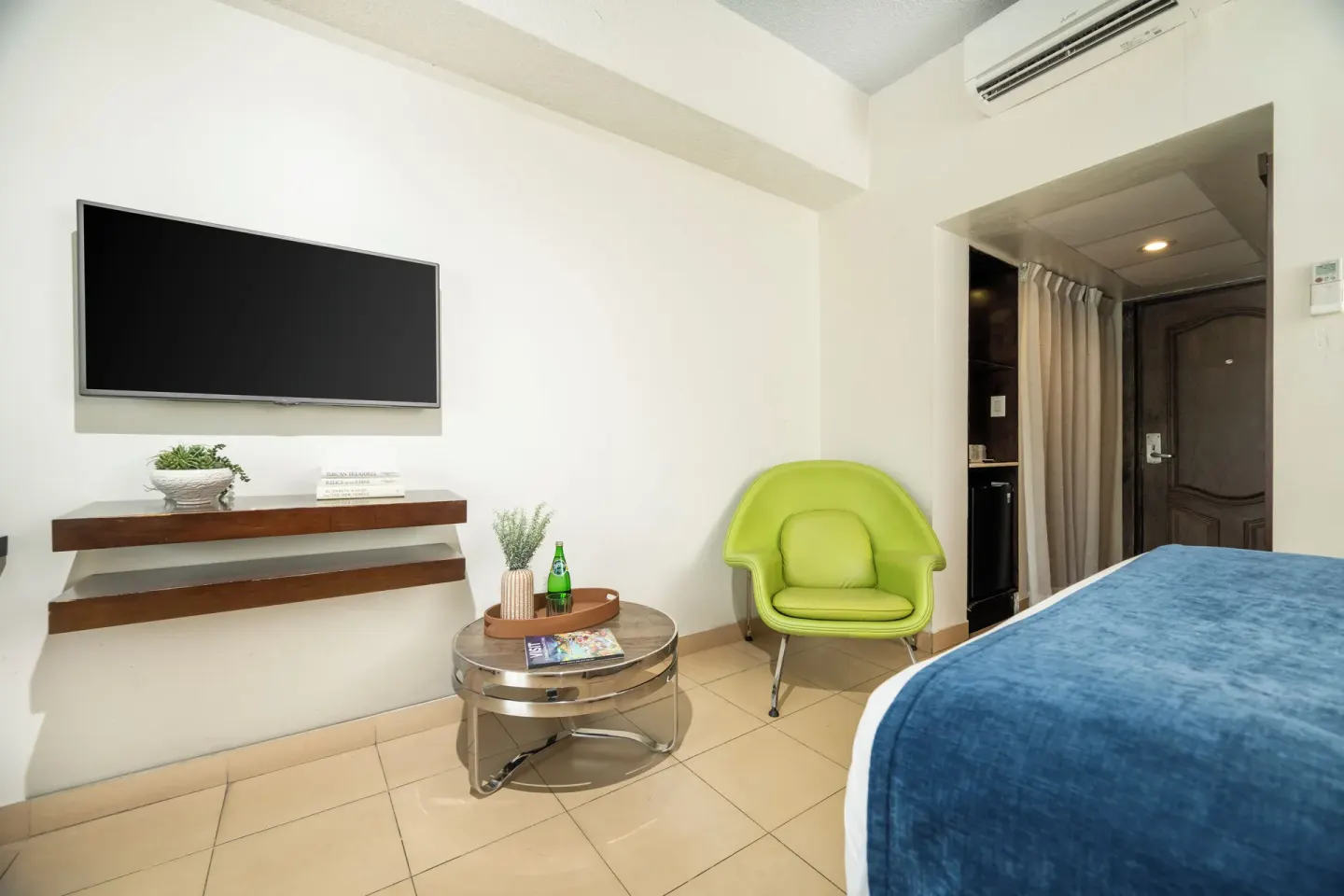 Standard Room with bed, wall TV, green chair, and entry door at Windward Passage Hotel.