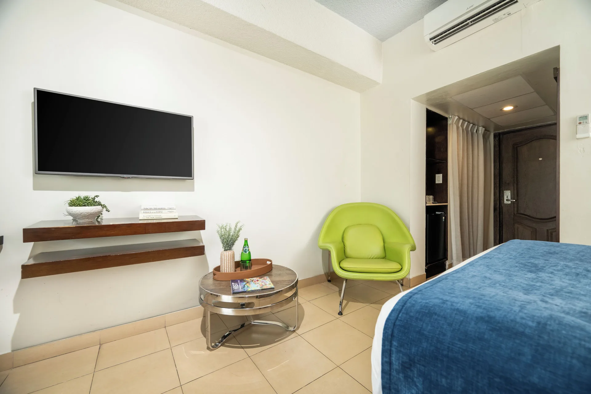 Standard Room with bed, wall TV, green chair, and entry door at Windward Passage Hotel.