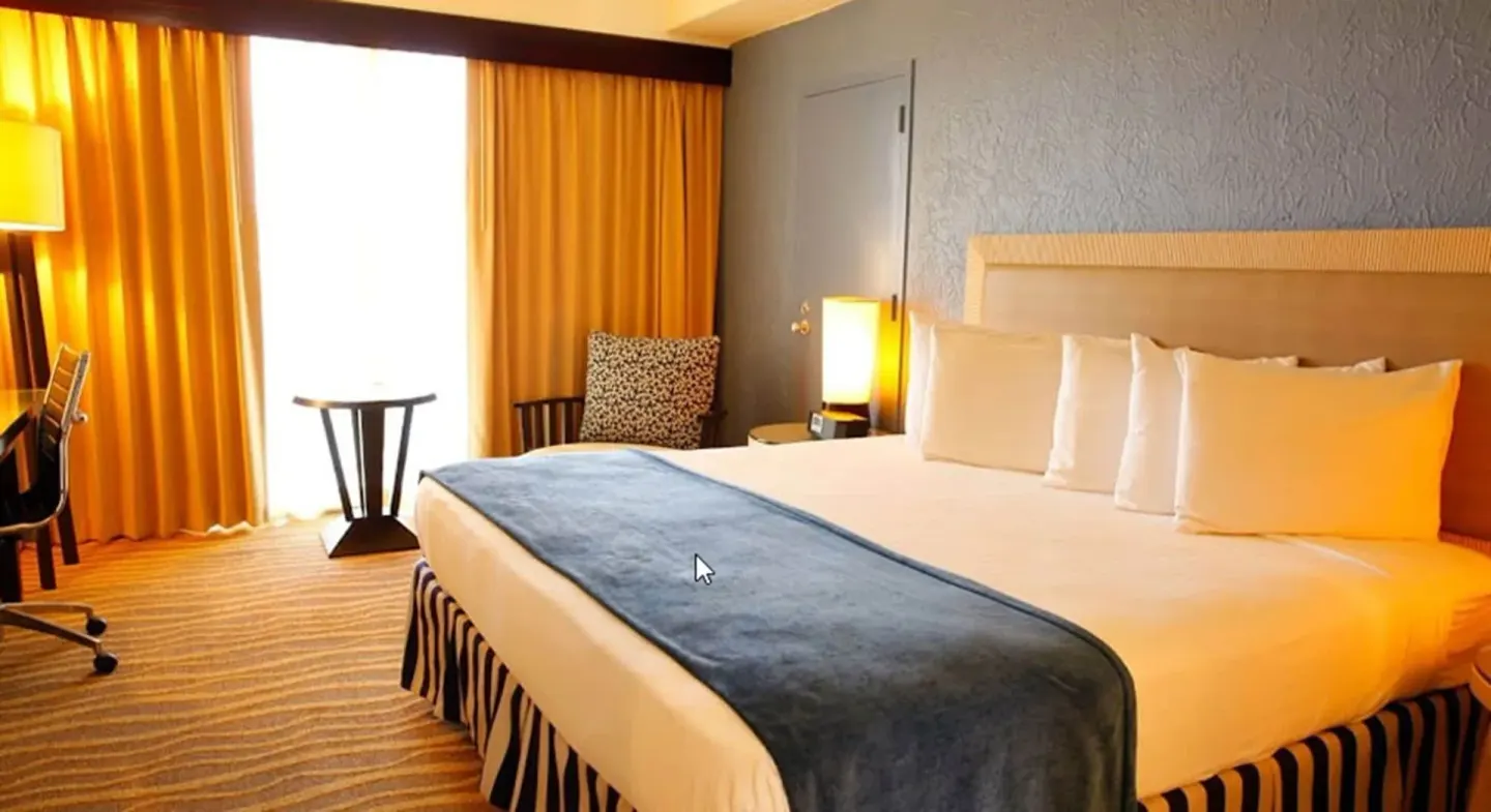 Standard Room king bed with desk, chair, curtains, and small table at Windward Passage Hotel.