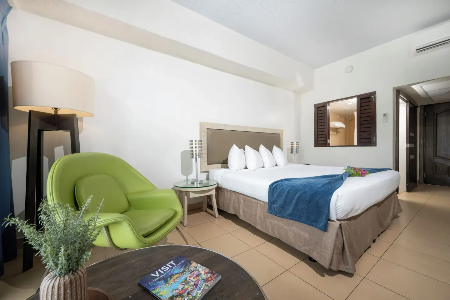 Standard room with king bed, green chair, lamp and entry at Windward Passage Hotel.