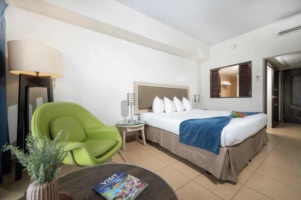 Standard room with king bed, green chair, lamp and entry at Windward Passage Hotel.