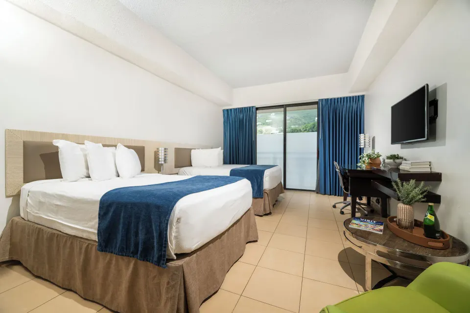 Standard Room with two beds, desk, TV, blue curtains, and round table at Windward Passage Hotel.