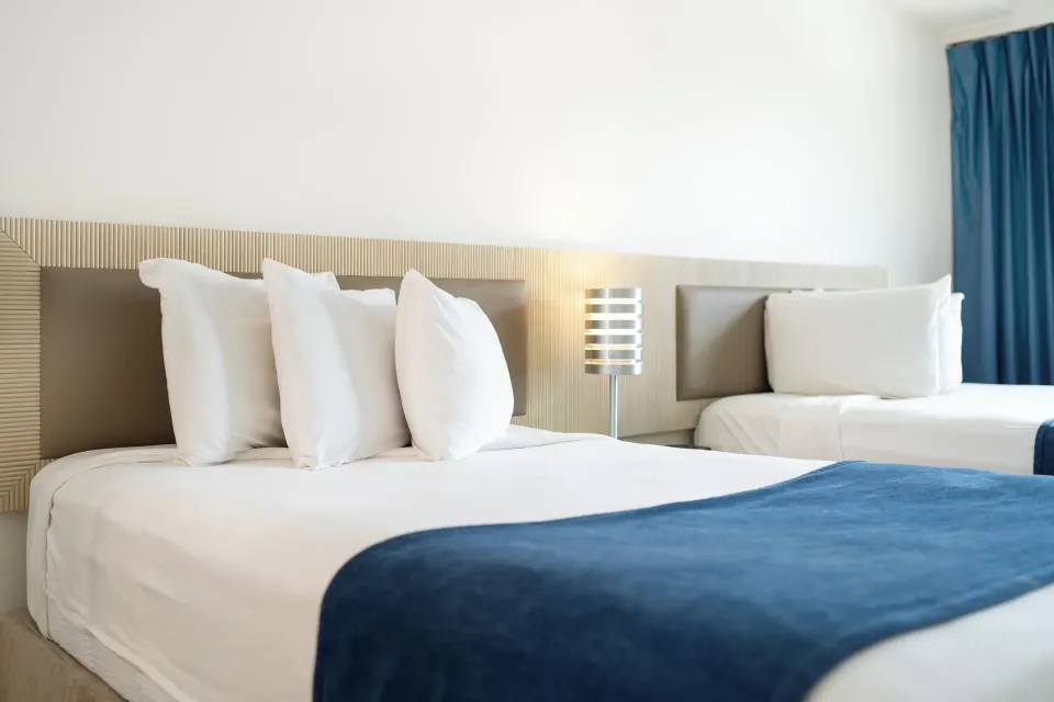 Close view of two Standard Room beds with white pillows and blue runners at Windward Passage Hotel.