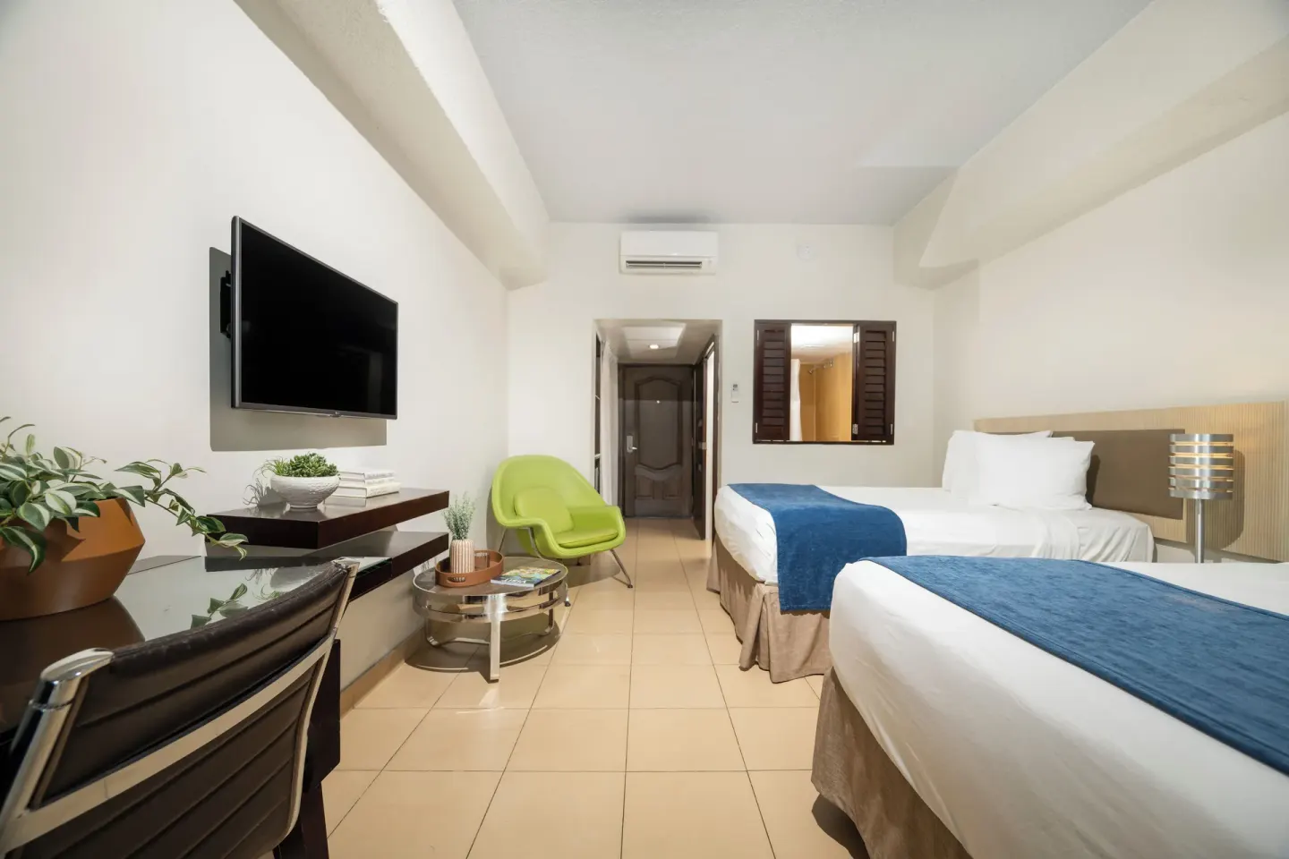 Standard Room with two beds, wall TV, desk chair, and green lounge chair at Windward Passage Hotel.