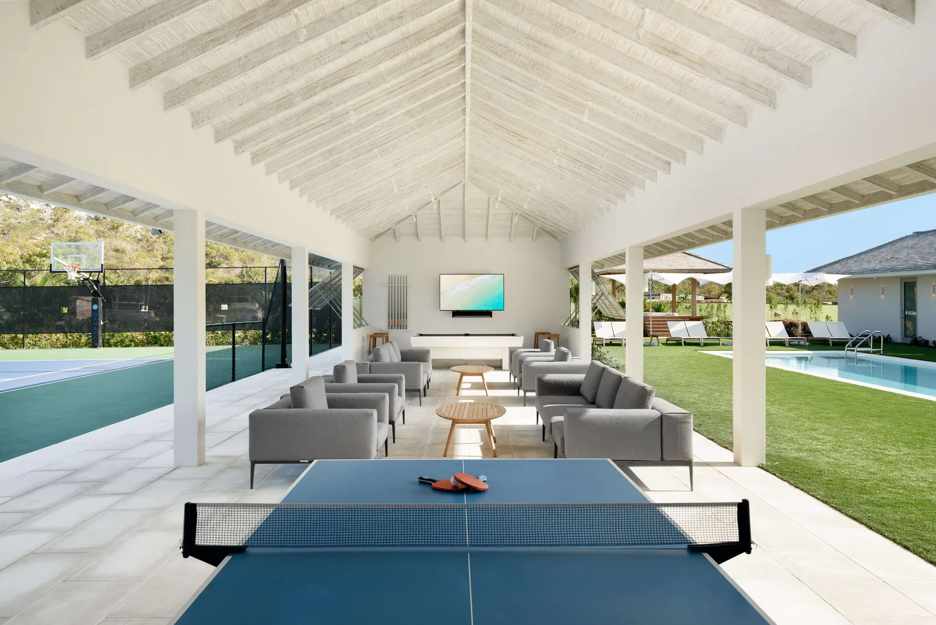Covered games lounge with ping-pong, seating, tennis court and pool at Wymara Resort and Villas.