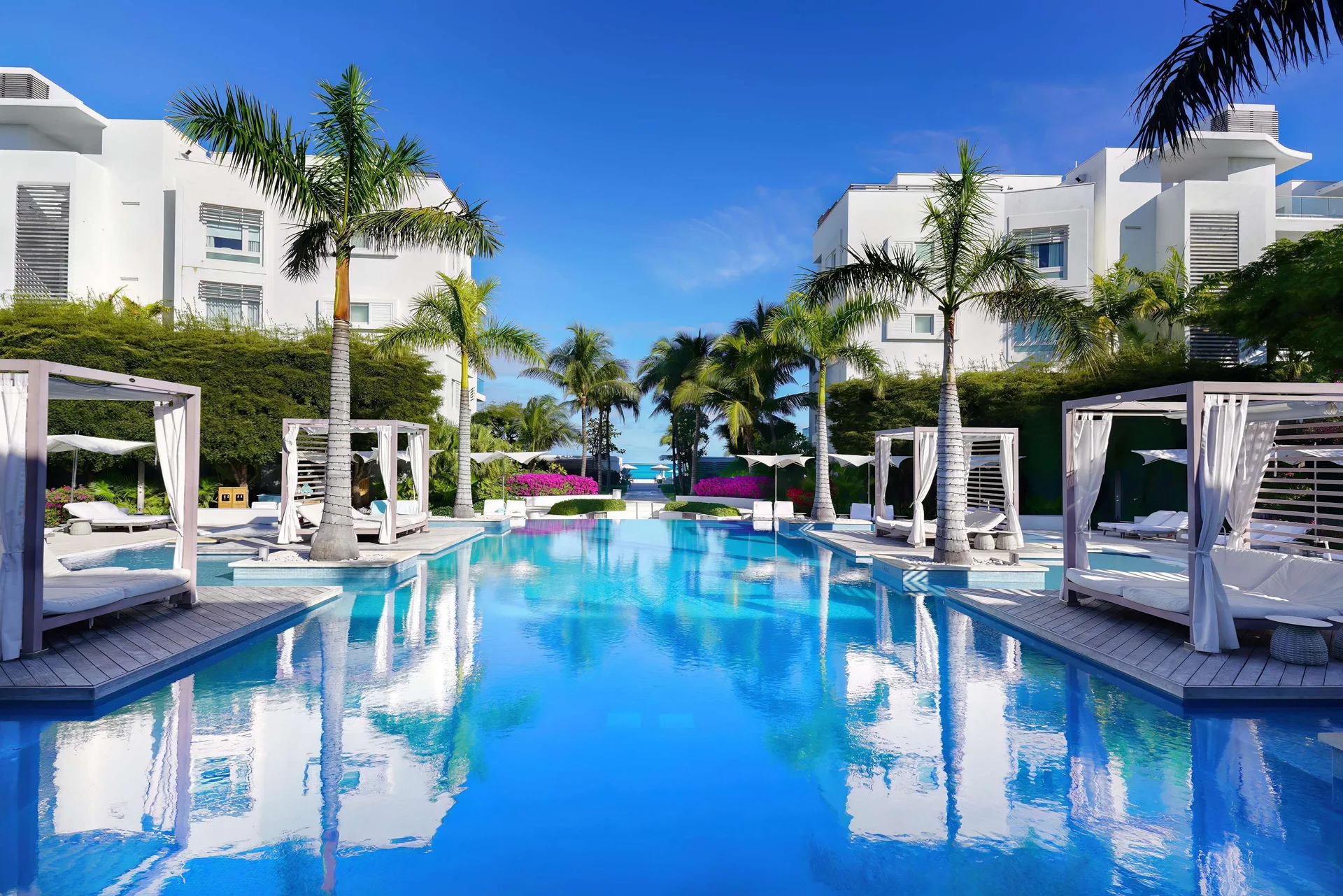 Daytime pool lined with cabanas, palms, and white buildings at Wymara Resort and Villas.