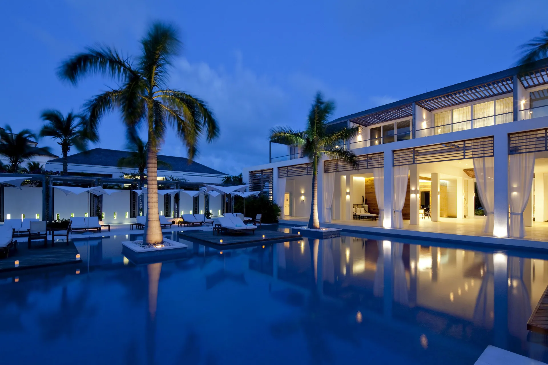 Evening pool with illuminated palms and white resort buildings at Wymara Resort and Villas.