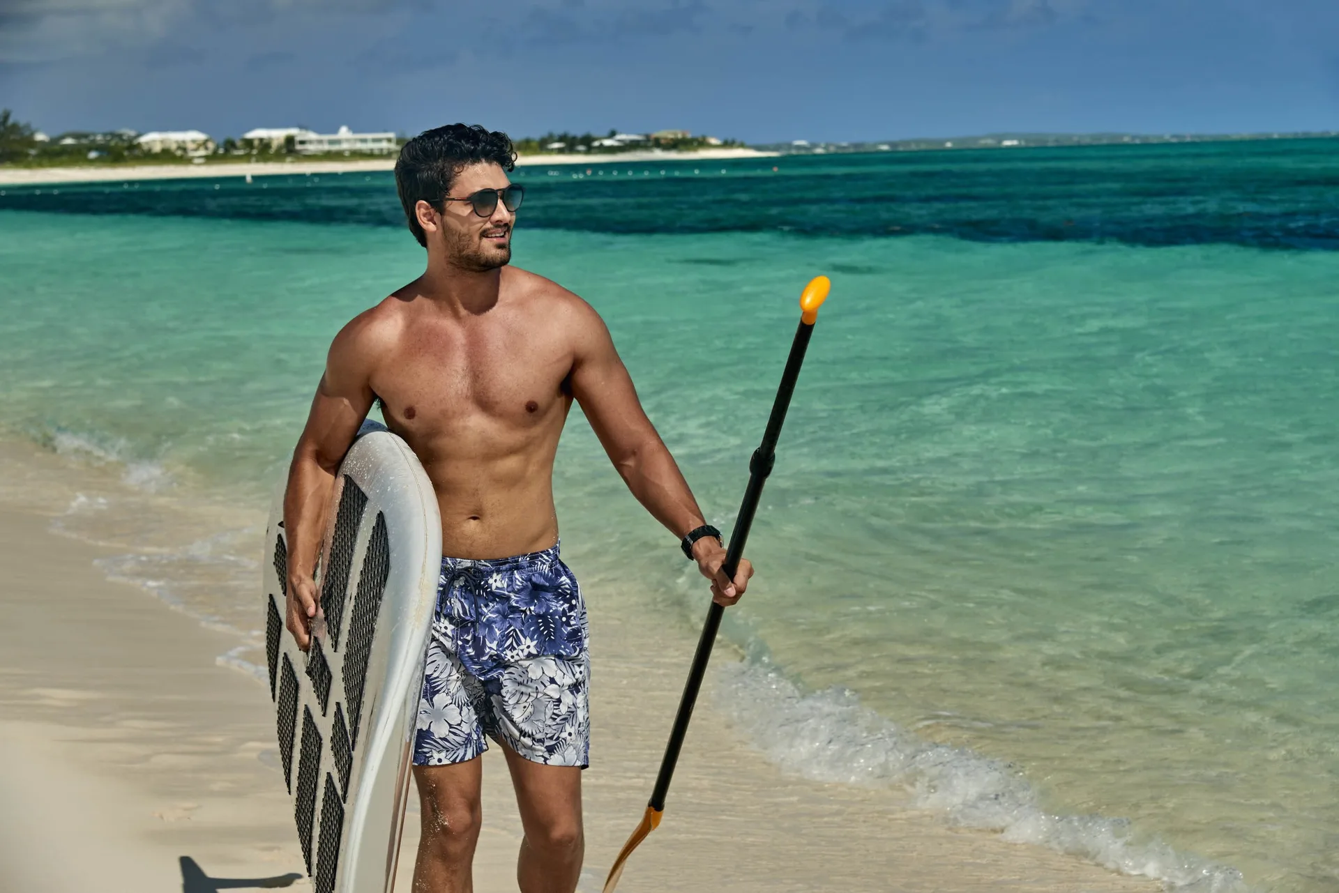 Man carrying a paddleboard and paddle along the shoreline at Wymara Resort and Villas.