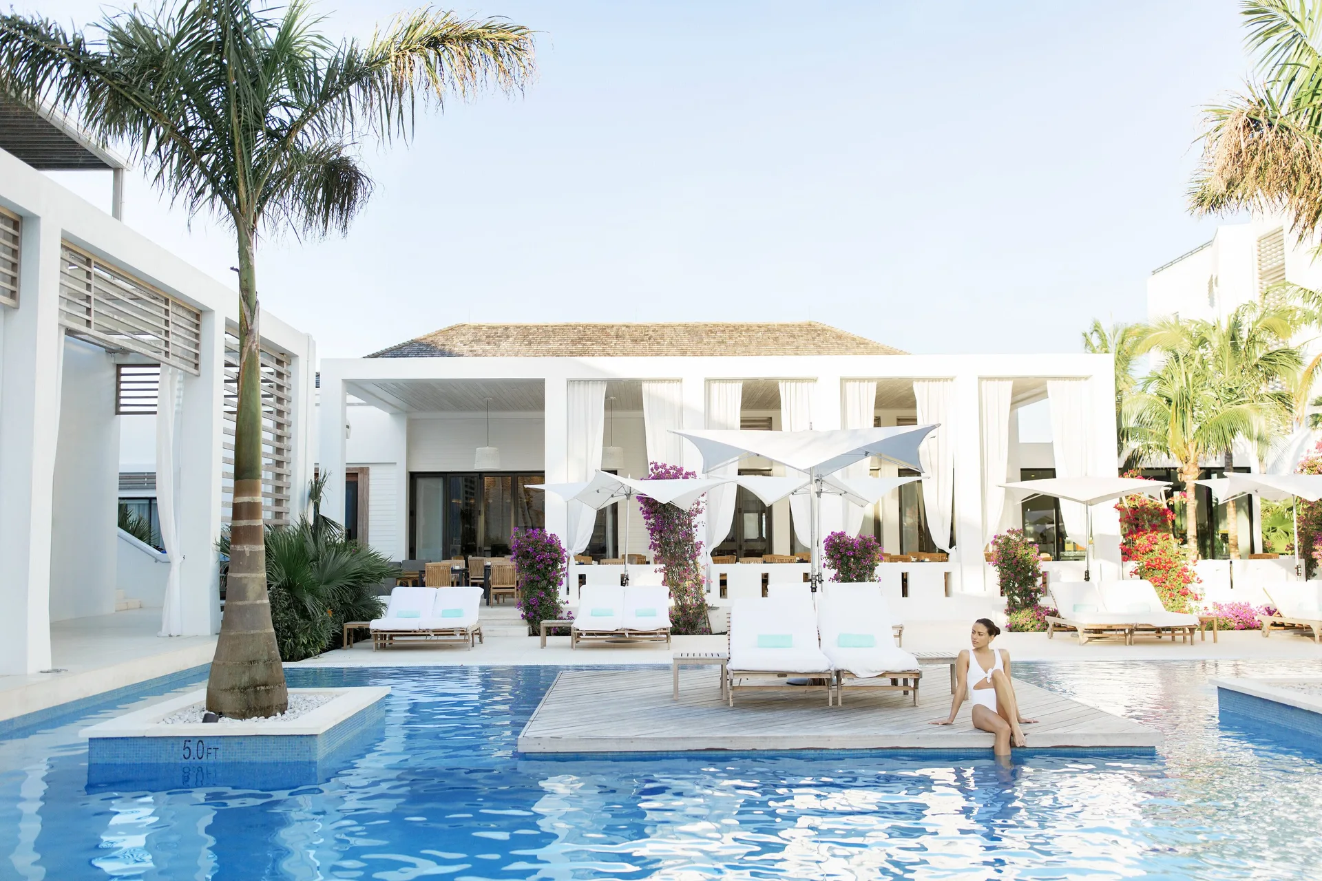 Guest sitting on a pool platform with loungers and palms at Wymara Resort and Villas.