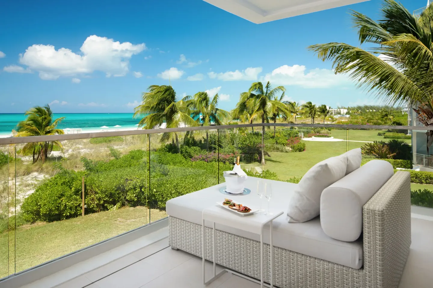 Grand Suite oceanfront balcony with cushioned lounger and palm-lined beach view at Wymara Resort and Villas.