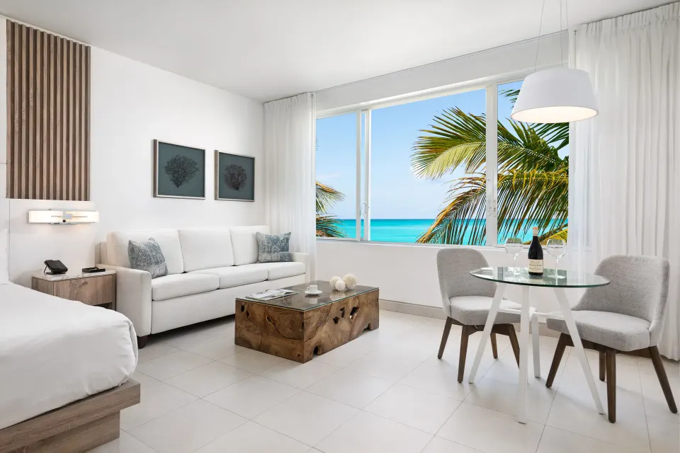 Grand Suite oceanfront living area with bed, sofa, dining table and sea view at Wymara Resort and Villas.