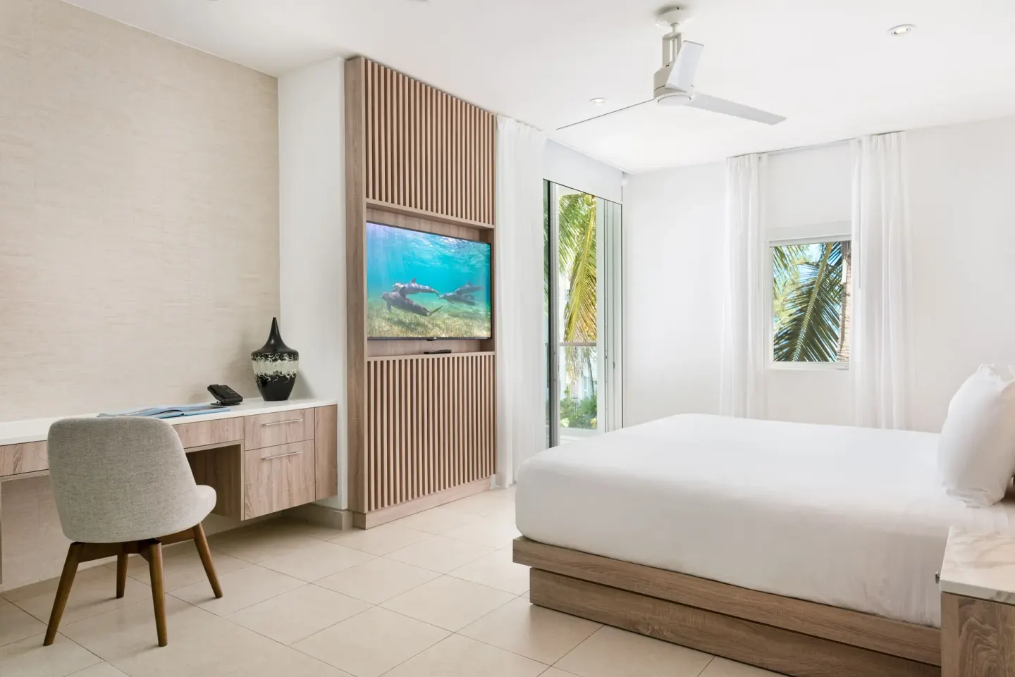 Studio Ocean View king bed, desk, TV, and palm-framed windows at Wymara Resort and Villas.