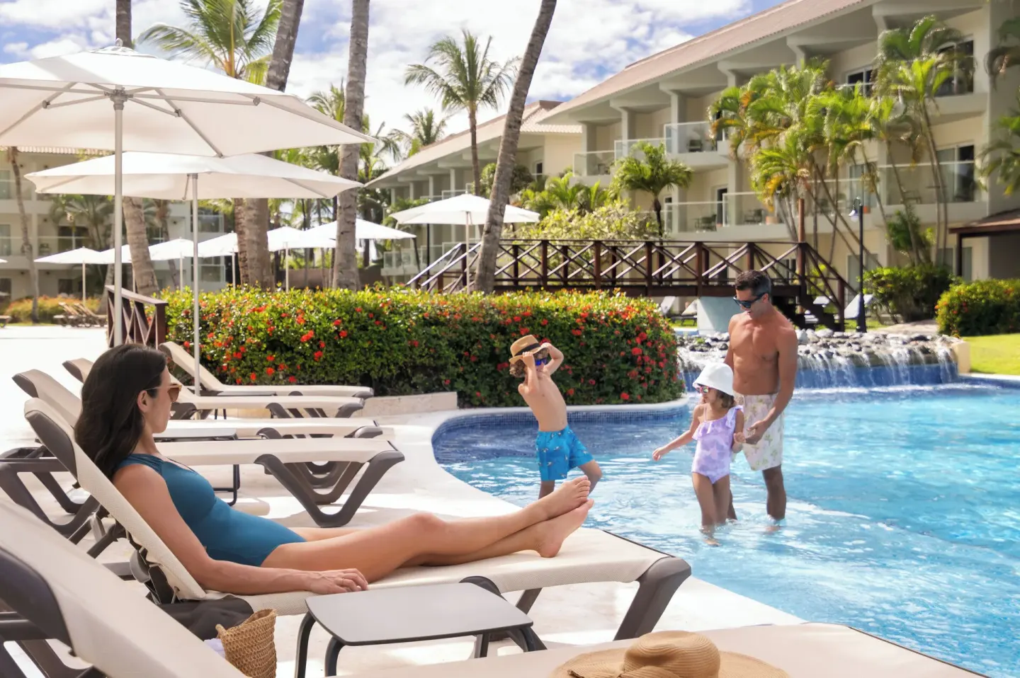 Family relaxing by a resort pool with loungers at Wyndham Alltra Punta Cana.