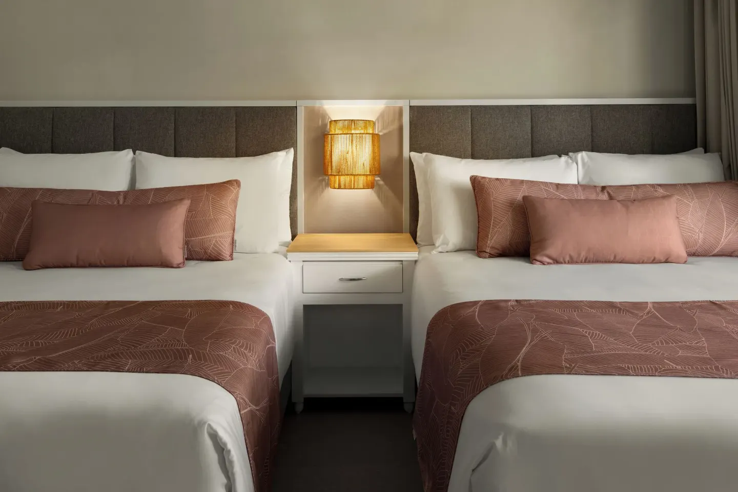 Two guest room beds with pink accents and a wall lamp at Wyndham Alltra Punta Cana.