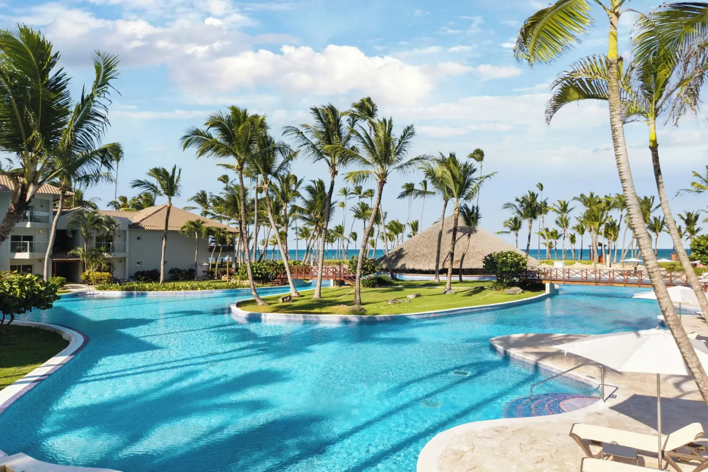 Lagoon-style pool with palms and ocean beyond at Wyndham Alltra Punta Cana.