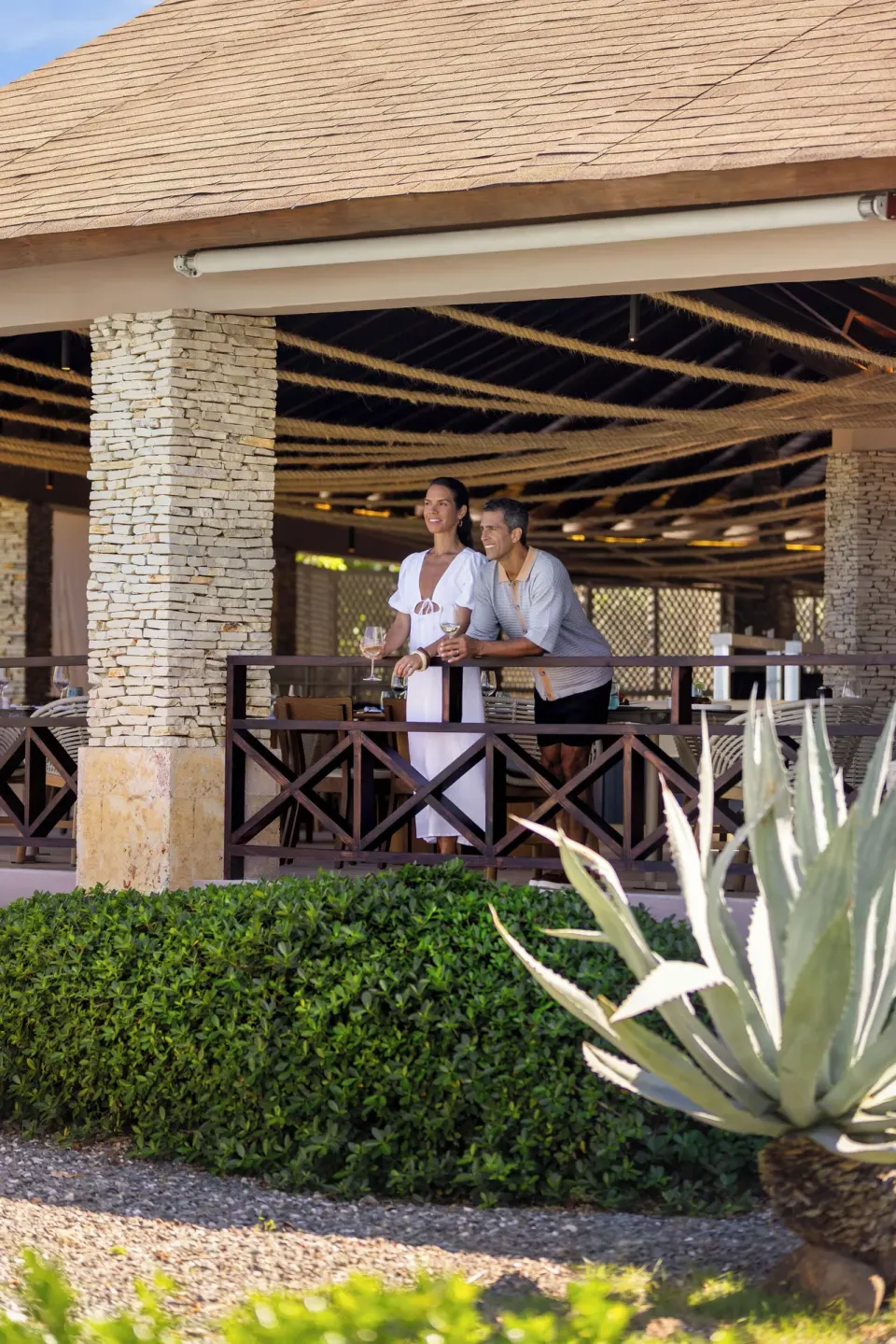 Couple stands with drinks on a shaded terrace at Wyndham Alltra Punta Cana.