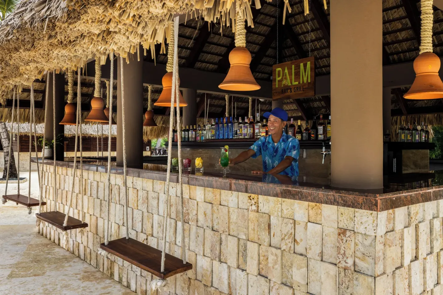 Palm Bar & Grill counter with swings and bartender at Wyndham Alltra Punta Cana.