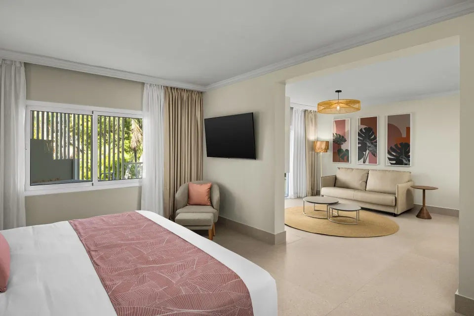 Junior suite with bed, sofa bed and tropical greenery at Wyndham Alltra Punta Cana.
