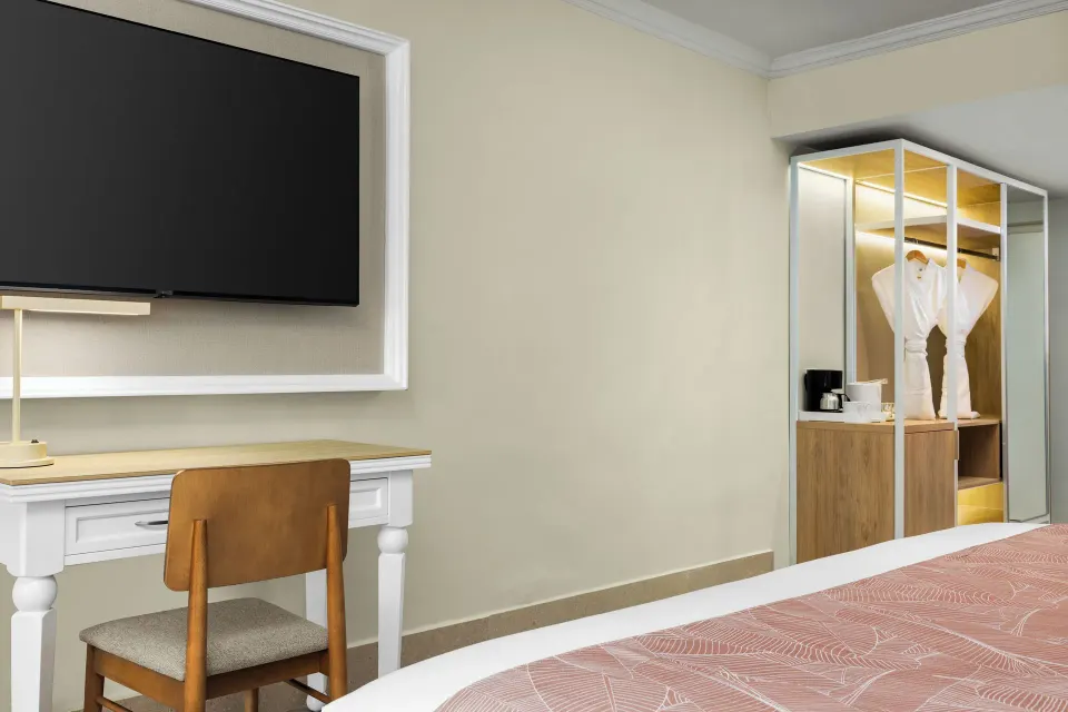 Standard tropical view room desk, TV, closet, and robe at Wyndham Alltra Punta Cana.