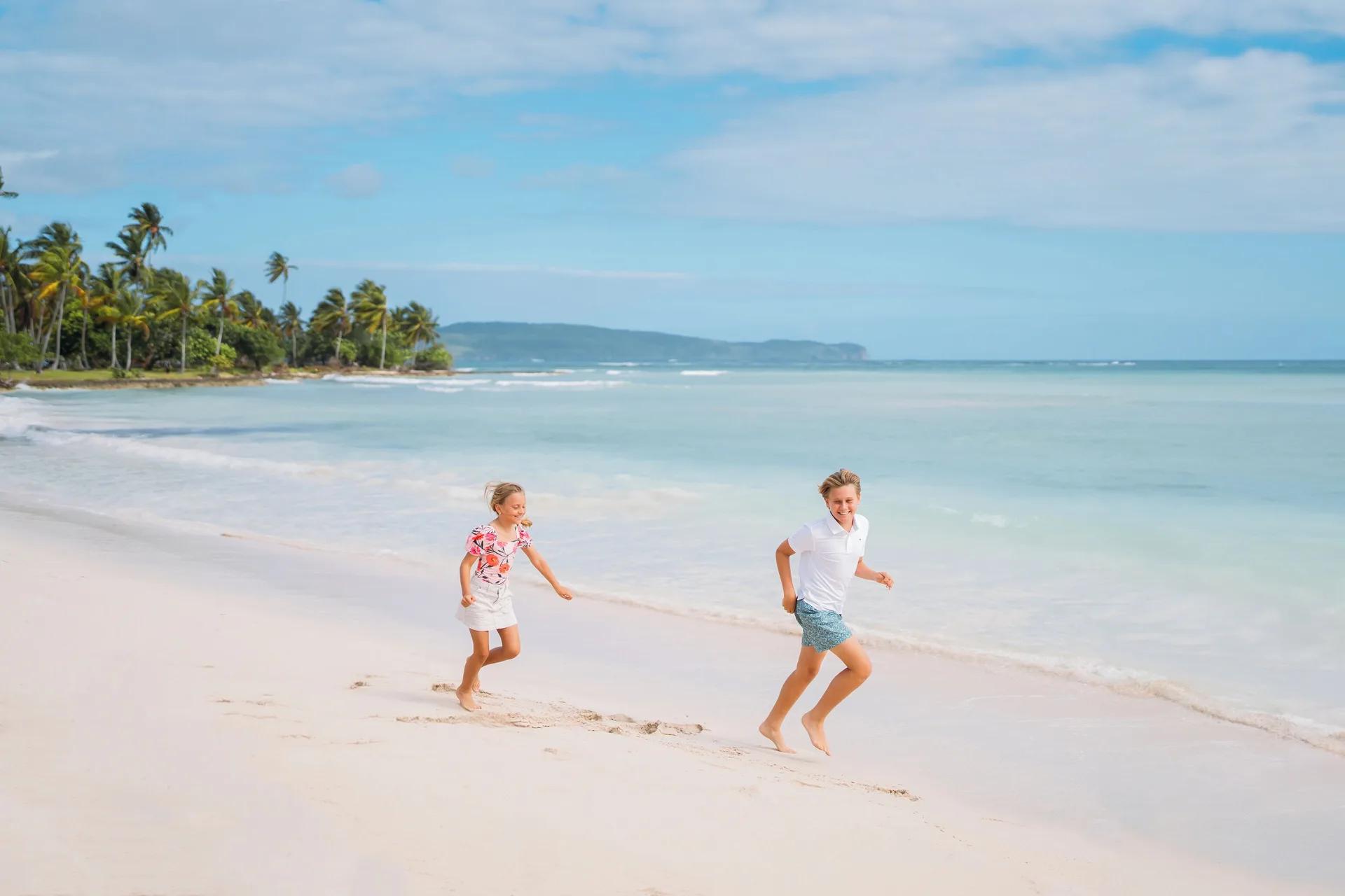 Two children run beside the surf on the beach at Wyndham Alltra Samana Resort.