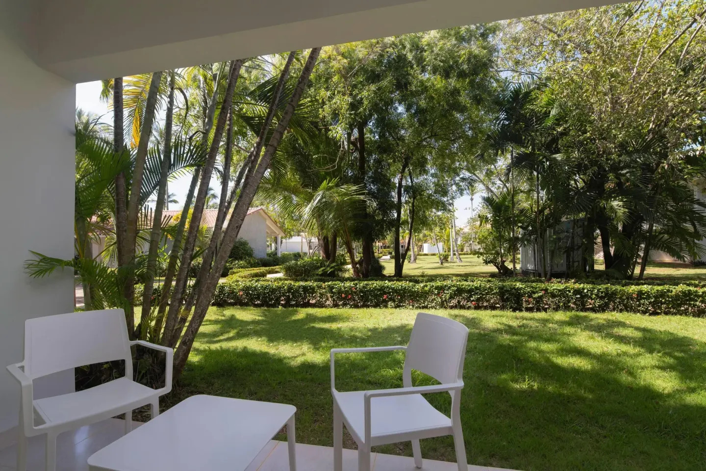 Covered patio with white chairs facing tropical gardens at Wyndham Alltra Samana Resort.