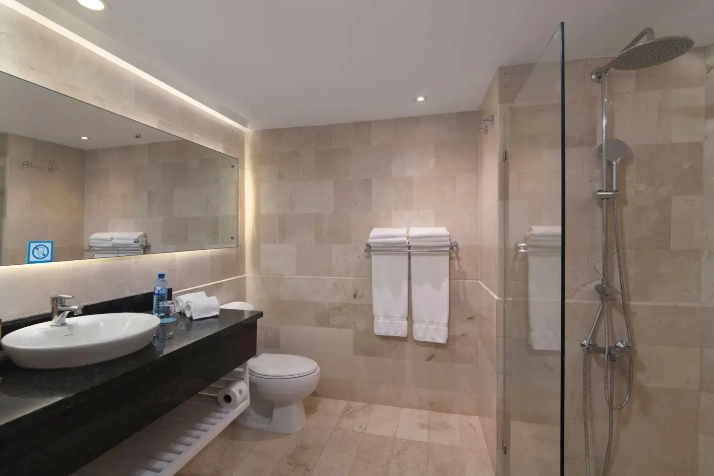 Bathroom with glass shower, vanity, towels, and stone tile at Wyndham Alltra Samana Resort.