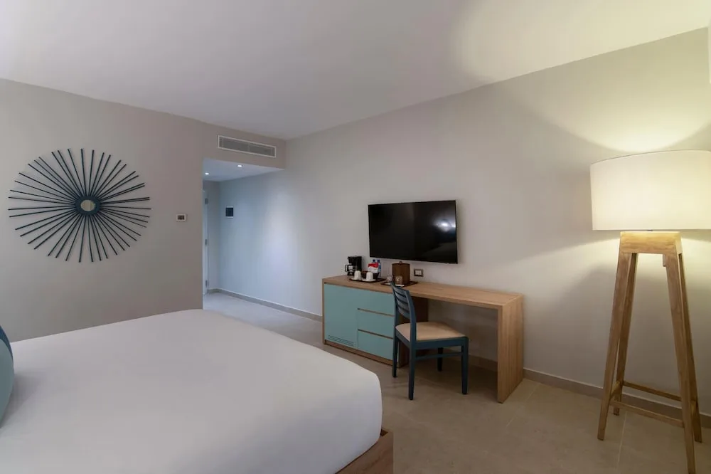 King-bed guest room with desk, TV and floor lamp at Wyndham Alltra Samana Resort.