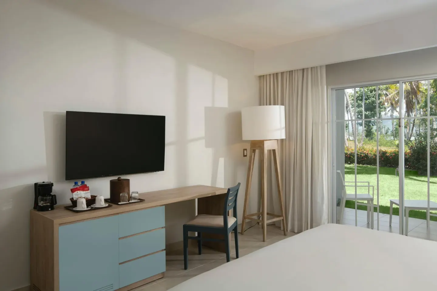 King-bed guest room with patio doors and garden beyond at Wyndham Alltra Samana Resort.