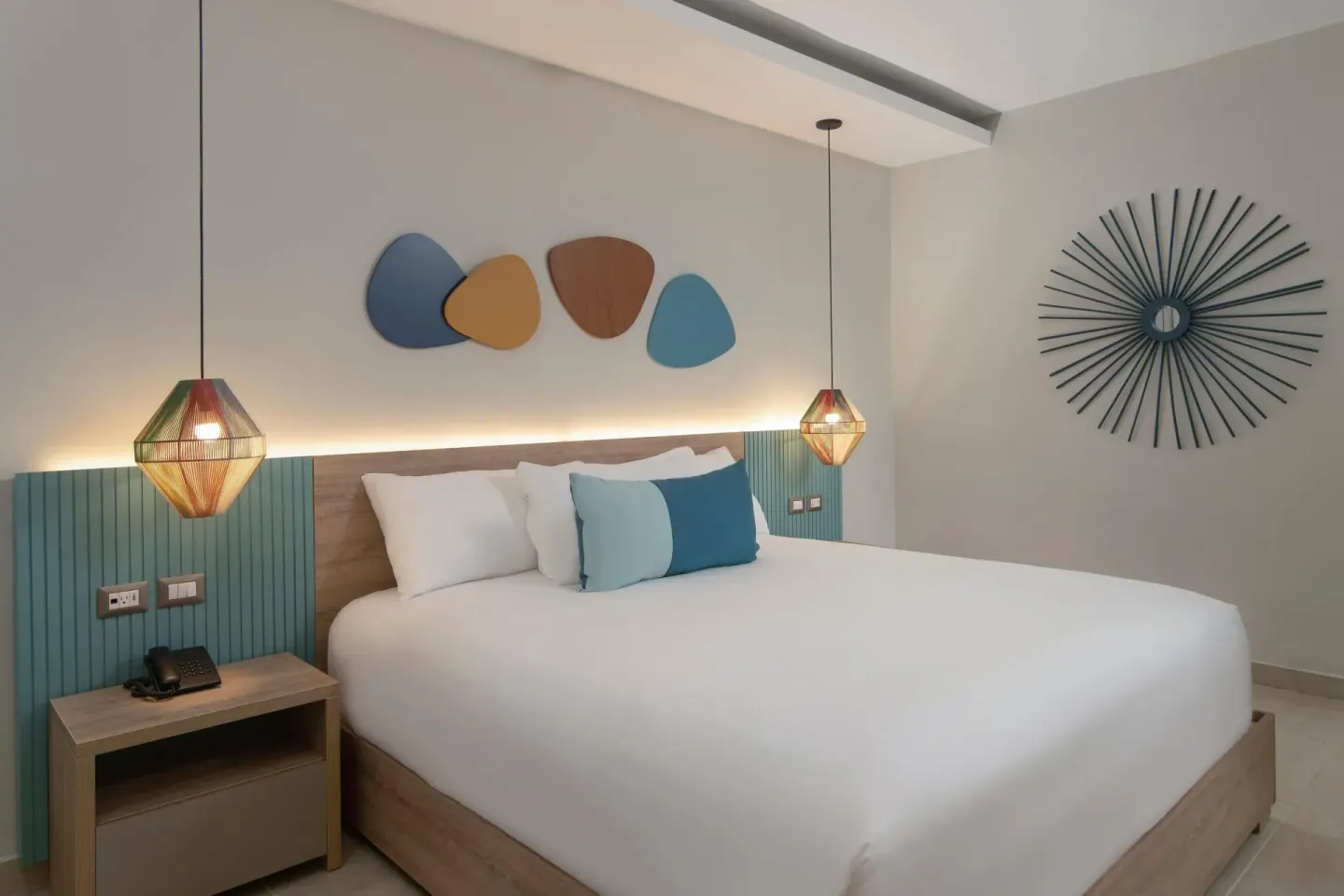 King-bed guest room with pendant lights and colorful wall art at Wyndham Alltra Samana Resort.