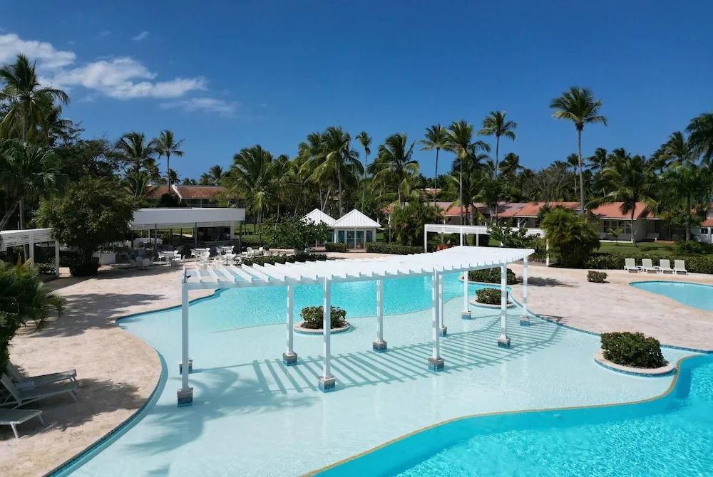 Large resort pool with white pergolas and palm trees at Wyndham Alltra Samana Resort.