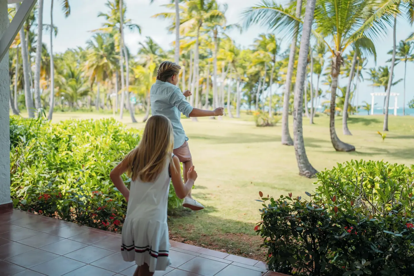 Children looking across palm-filled lawns toward the beach at Wyndham Alltra Samana Resort.
