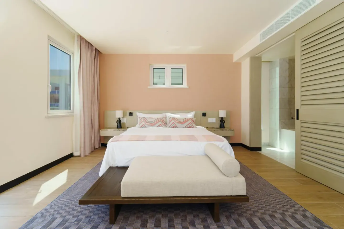 King bed guest room at Wyndham Grand Barbados Sam Lords Castle with pink accent wall and bench.