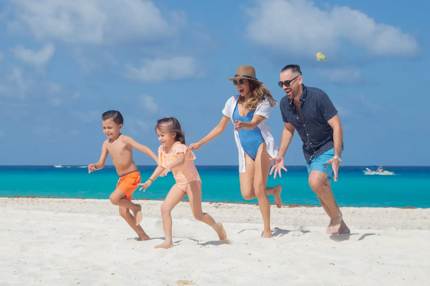 Family running on the beach by turquoise water at Wyndham Grand Cancun Resort & Villas.